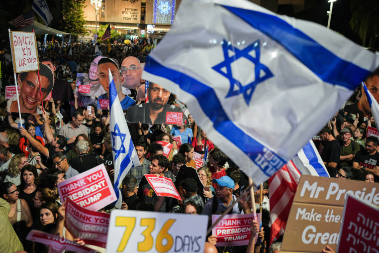 A crowd of protestors, some people wave large Israeli flags and posters