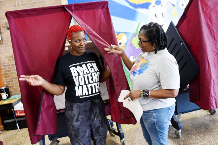 Pamela Evans walks out of a voting booth and is greeted by a poll worker, she wears a black t-shirt that reads "Black Voters Matter" in white lettering