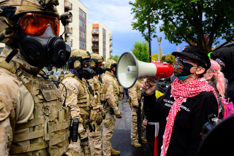 A protester with a bullhorn in front of federal agents.