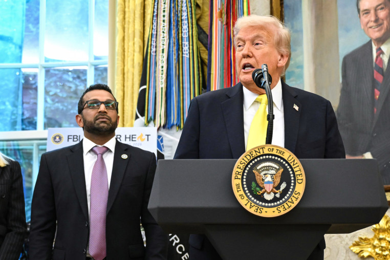 Kash Patel, left, and Donald Trump, who is standing at a podium and speaking