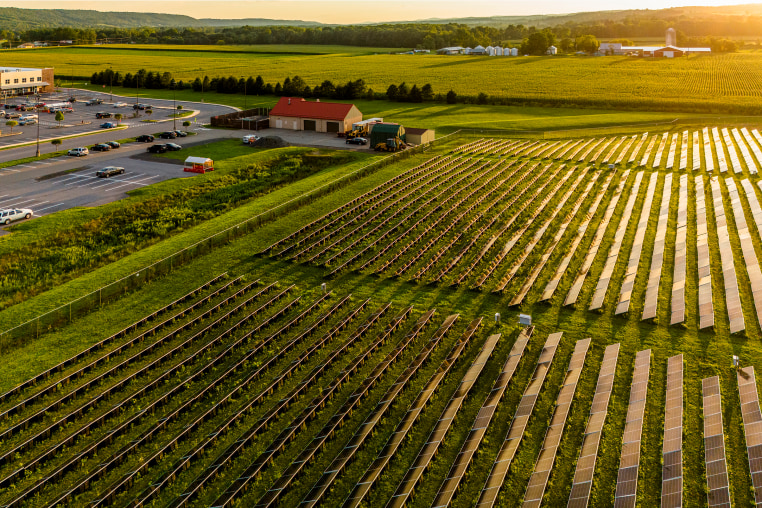 Sunset beams reflect in solar farm panels in Pennsylvania rolling farmlands and commercial zone in Brodheadsville, Poconos.