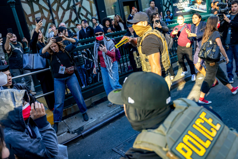 A Federal agent pulls out his taser as law enforcement conduct a raid on street vendors during rush hour. New Yorkers are seen witnessing the attempted detainments began protesting and attempted to block agents.