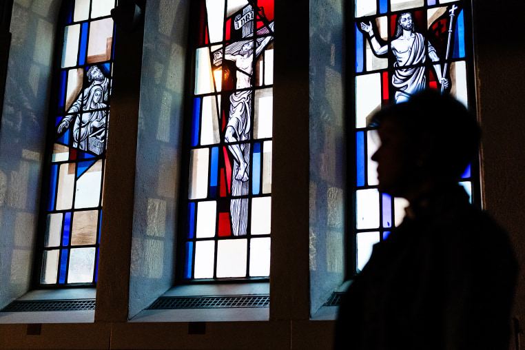 Pastor stands silhouetted by stained glass windows.
