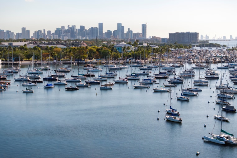 A drone view shows sailboats moored next to the Coconut Grove Sailing Club and the downtown skyline in Miami