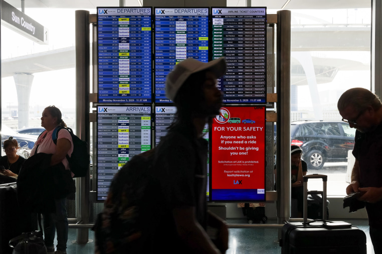 Travelers walk past the flight information display system at Los Angeles International Airport/