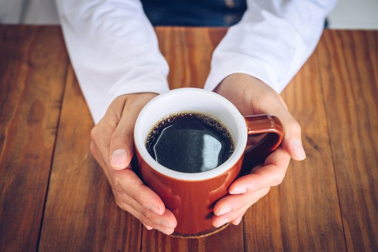 Hands holding a mug of black coffee