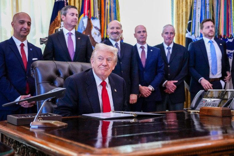 President Trump sits at his desk at the White House surrounded by others.