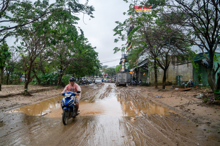 A person on a motorbike drives atop a muddy road over a puddle