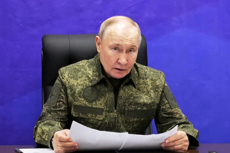 Russian President Vladimir Putin sat holding a papers against a purple background