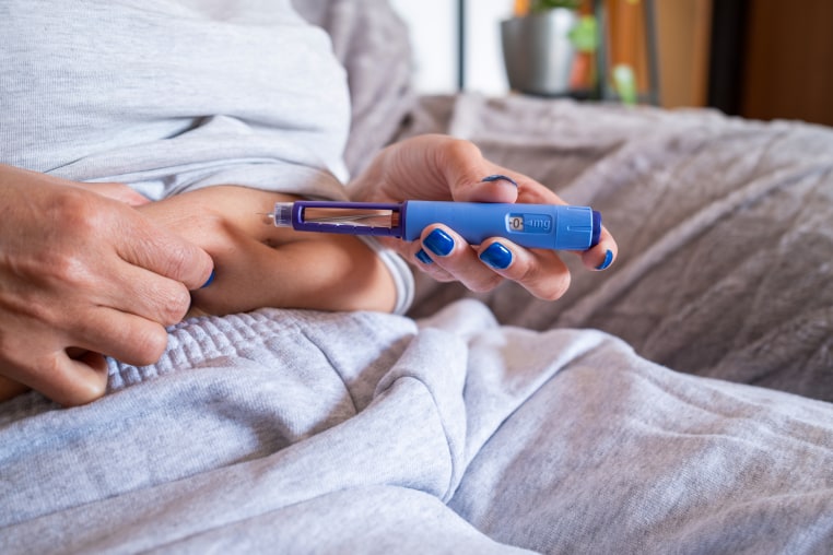 Unrecognizable mature overweight diabetic woman injecting a syringe of semaglutide into her stomach.