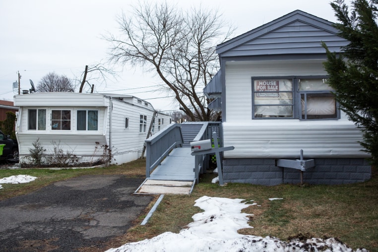 A '"for sale" sign is seen in a window of a mobile home