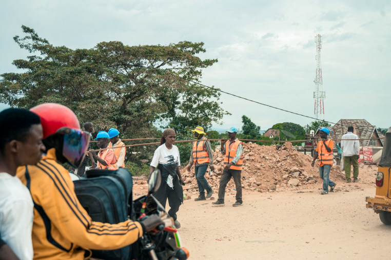 People walk and ride motorbikes along a dirt road