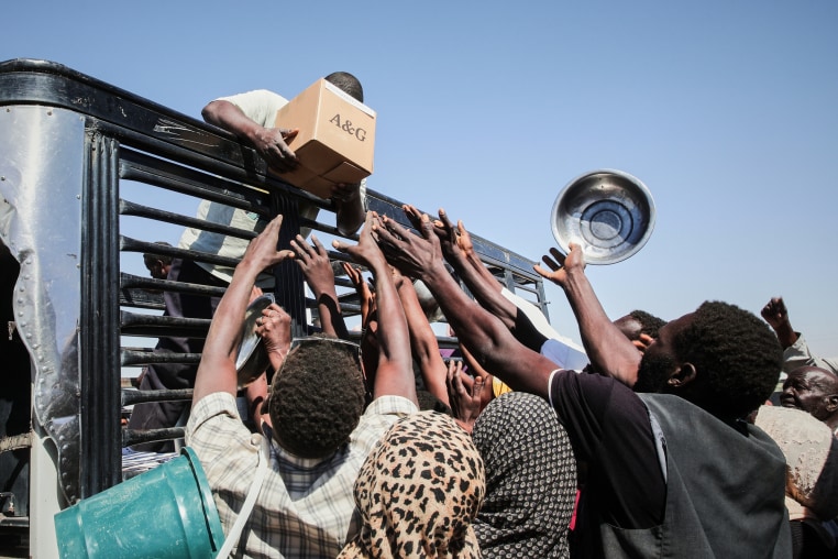People reach towards a box of food