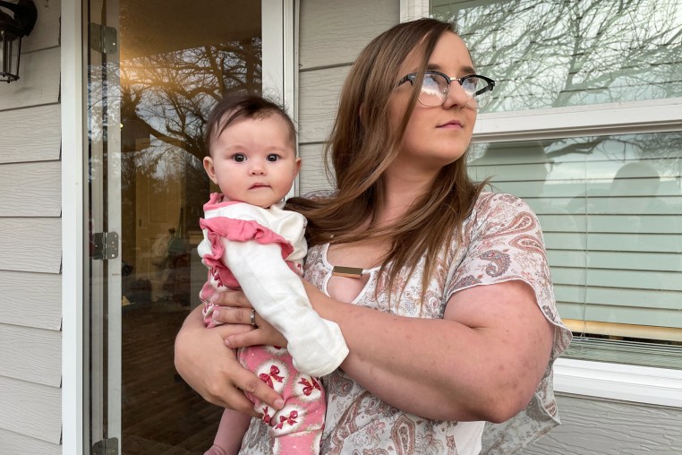 A mother holds a baby outside of a house
