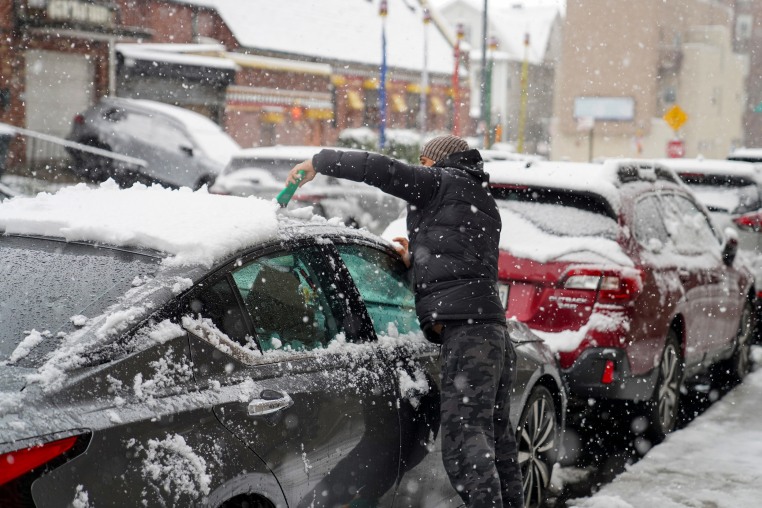 A person cleans the snow from their car.