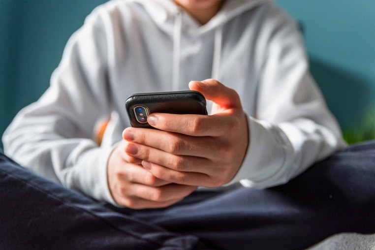 Close up of hands of teen boy in white sweater texting on phone.