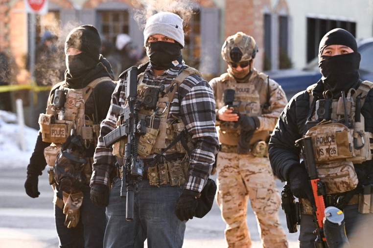 Image: Federal agents look on as demonstrators gather near the site of where state and local authorities say a man was shot