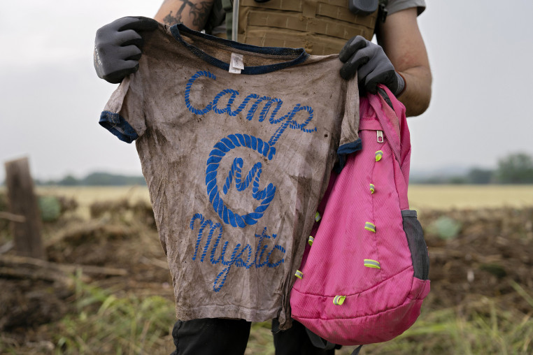 A search and rescue volunteer holds a T-shirt and backpack with the words Camp Mystic on them.
