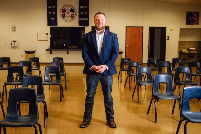 Taylor Rehmet stands between rows of chairs in an auditorium