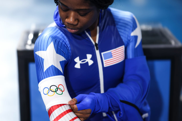Erin Jackson puts on a white arm band with a graphic showing Olympic rings on it