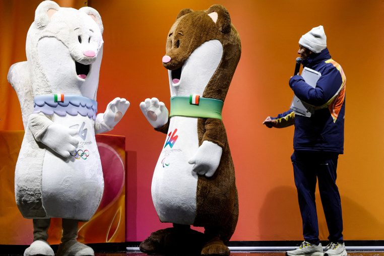 Two large stoat mascots, one white and one brown, stand on stage next to a person holding a microphone