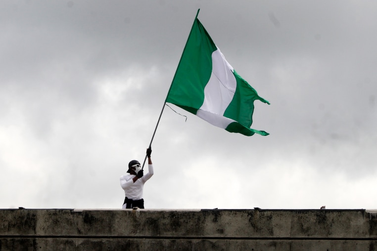 A person on the roof of a building waves a Nigerian flag