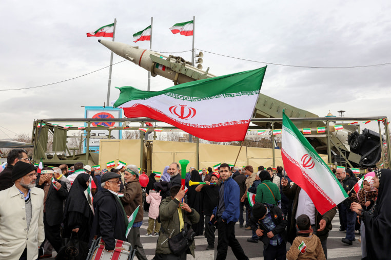 People walk with Iranian national flags near a ballistic missile launch vehicle