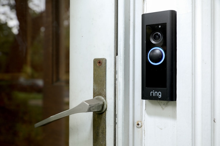 A black Ring doorbell camera is mounted next to the handle of a glass door on the exterior of a house.