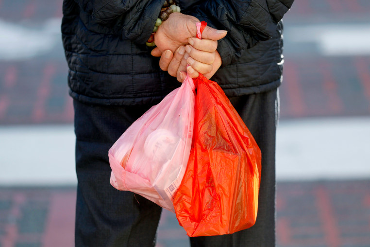 A pedestrian carries plastic shopping bags.