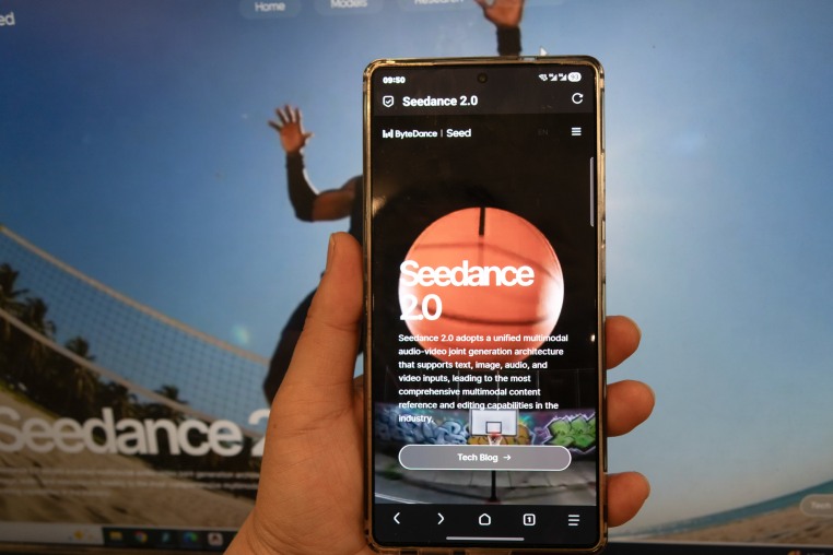 A hand holds up a mobile phone in front of a computer screen. Both read "Seedance 2.0".