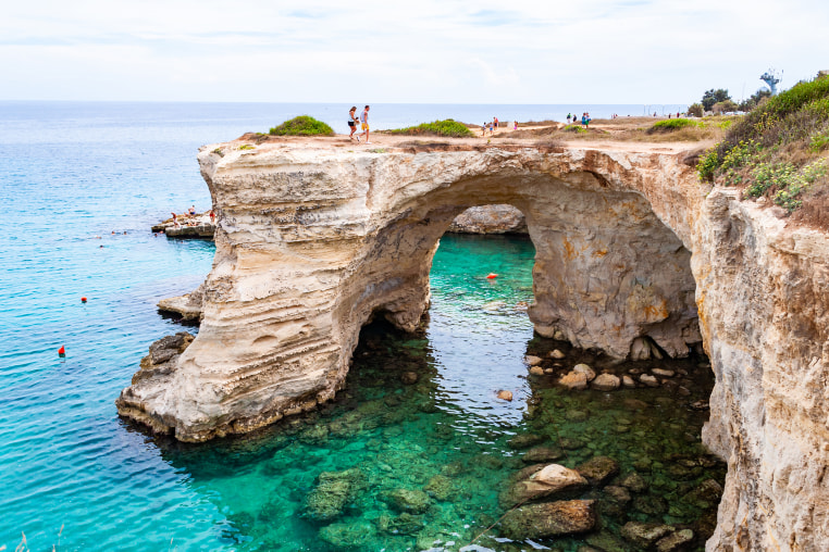 Tourists on the edge of rock. Torre Sant Andrea beach with its soft calcareous rocks and cliffs, sea stacks, small coves and the jagged coast landscape