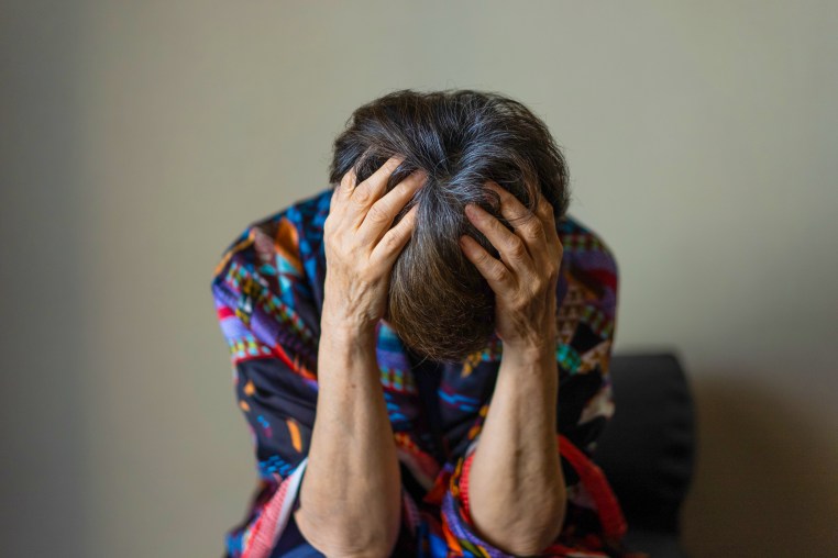 An old woman holding her head with both hands and slumped down