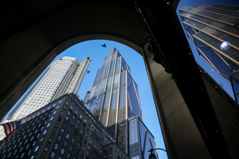 Birds fly past skyscrapers seen from a street-level view. 