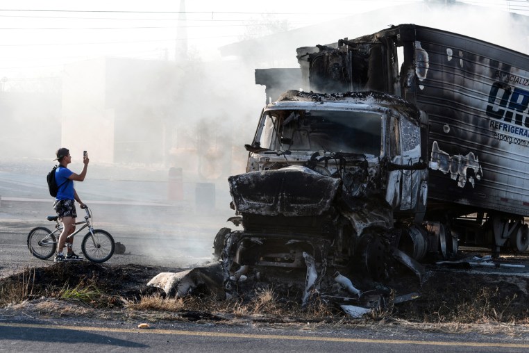 A man riding a bicycle takes a photo of a burned truck