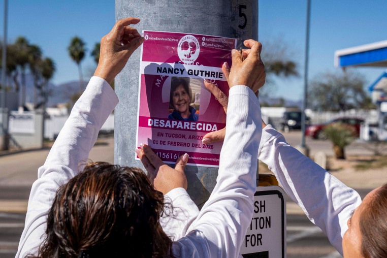A person puts up a missing poster of Nancy Guthrie on a pole outside