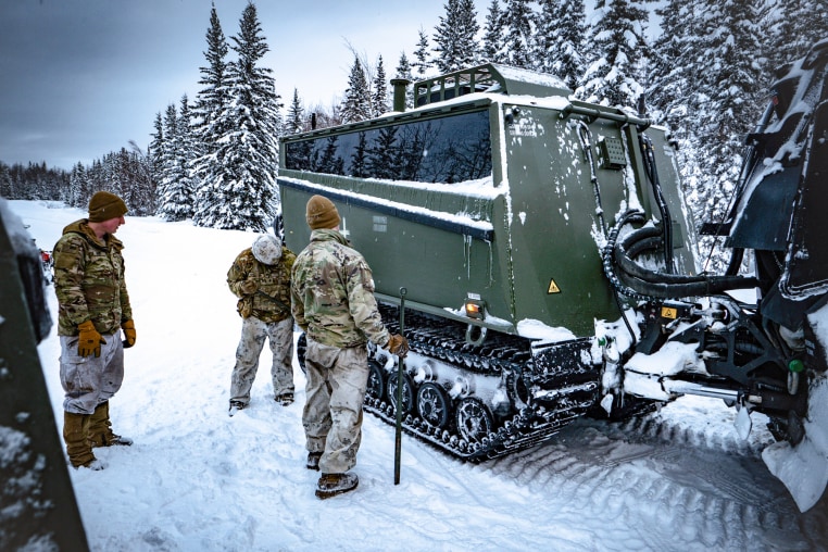 Soldiers from the 11th Airborne Division inspecting a Cold Weather-All Terrain Vehicle in the snow outside