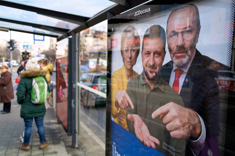 A billboard is seen at a bus stop, showing an AI image of Volodymyr Zelenskyy holding out his hand