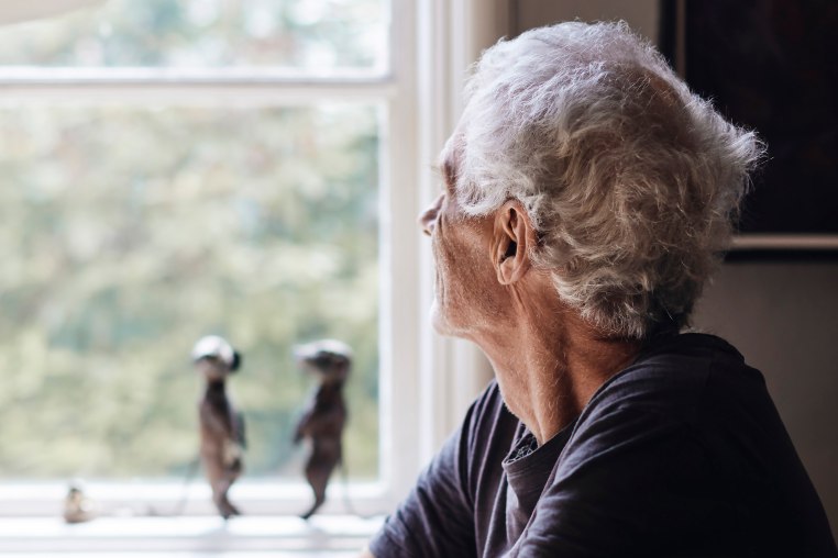 Image: Senior man looking through window while sitting at home