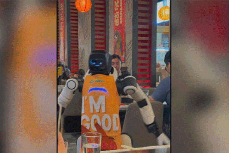 A robot wears an orange apron and has two hearts for eyes