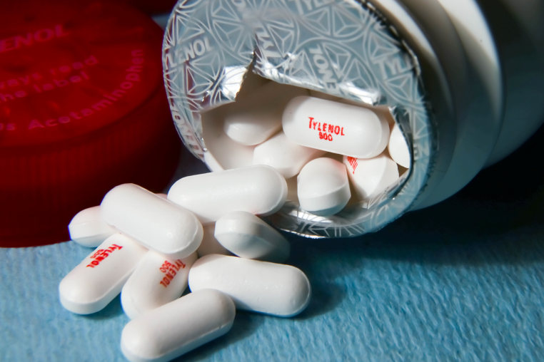 White tylenol pills lie outside a bottle tipped on its side.