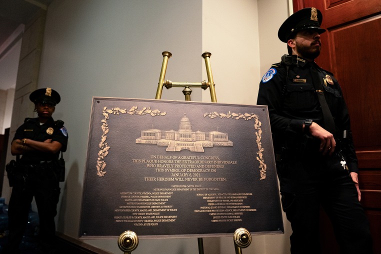 Two Capitol police officers stand on either side of a large metal plaque on display in a hallway.
