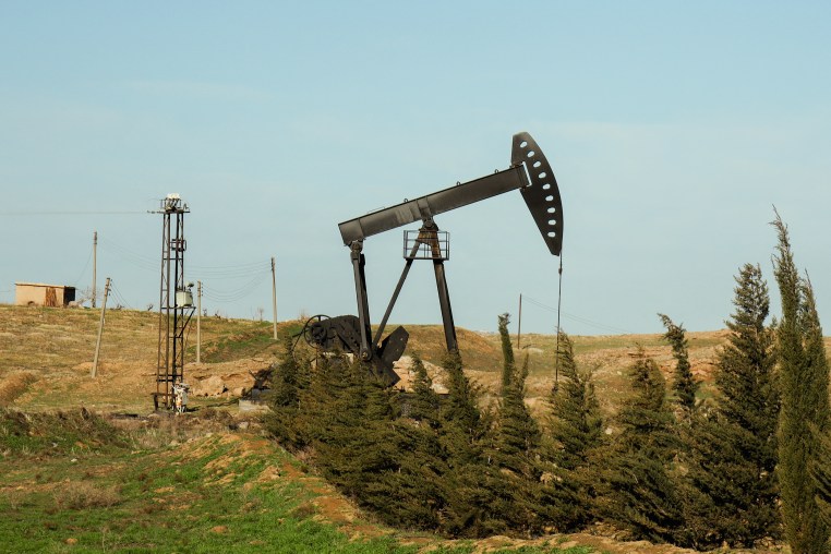 An oil pump jack rises above the horizon against a clear blue sky.