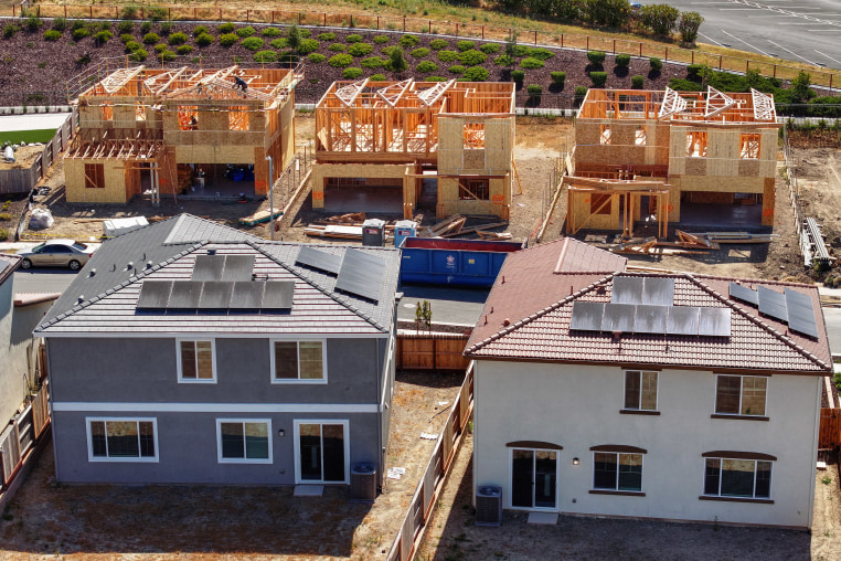 Three partially-built houses stand behind two finished houses with solar panels.