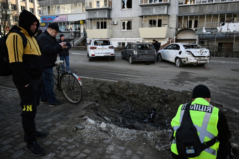 Residents look at a crater as police expert work at a site of a strike in the town of Brovary, near Kyiv, following a Russian missile and drone attack, on March 14.