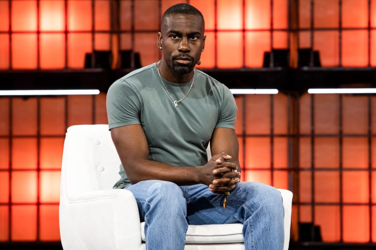 Deray Mckesson sits on a white couch on stage