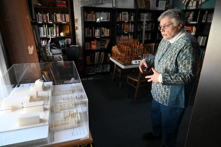 A woman stands in front of an architectural model encased in glass.