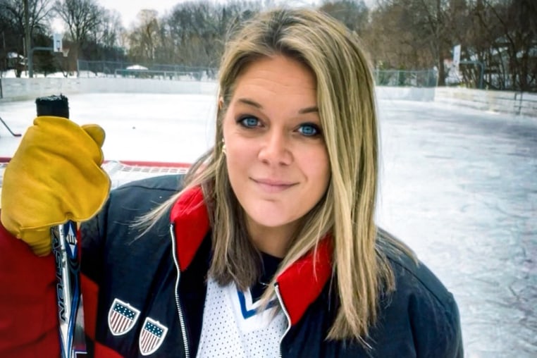 Jessi Pierce stands outside holding a hockey stick on an ice rink