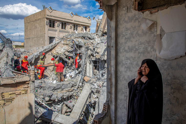 A woman speaks on the phone as emergency workers sift through rubble.