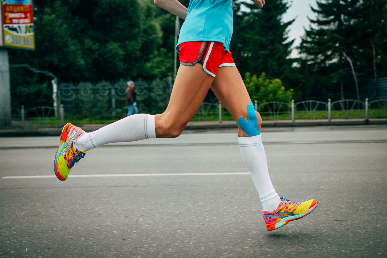 Image: A girl athlete running with her knees in blue kinesiology taping 