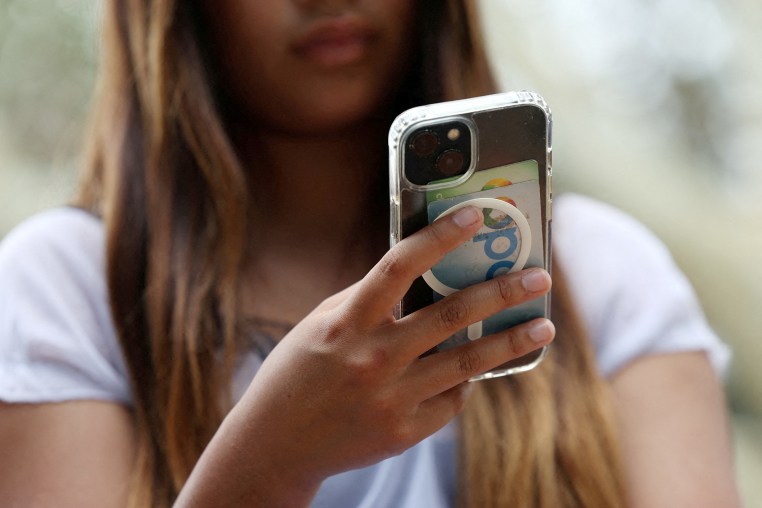 A teenager poses holding a mobile phone as law banning social media for users under 16 in Australia takes effect, in Sydney
